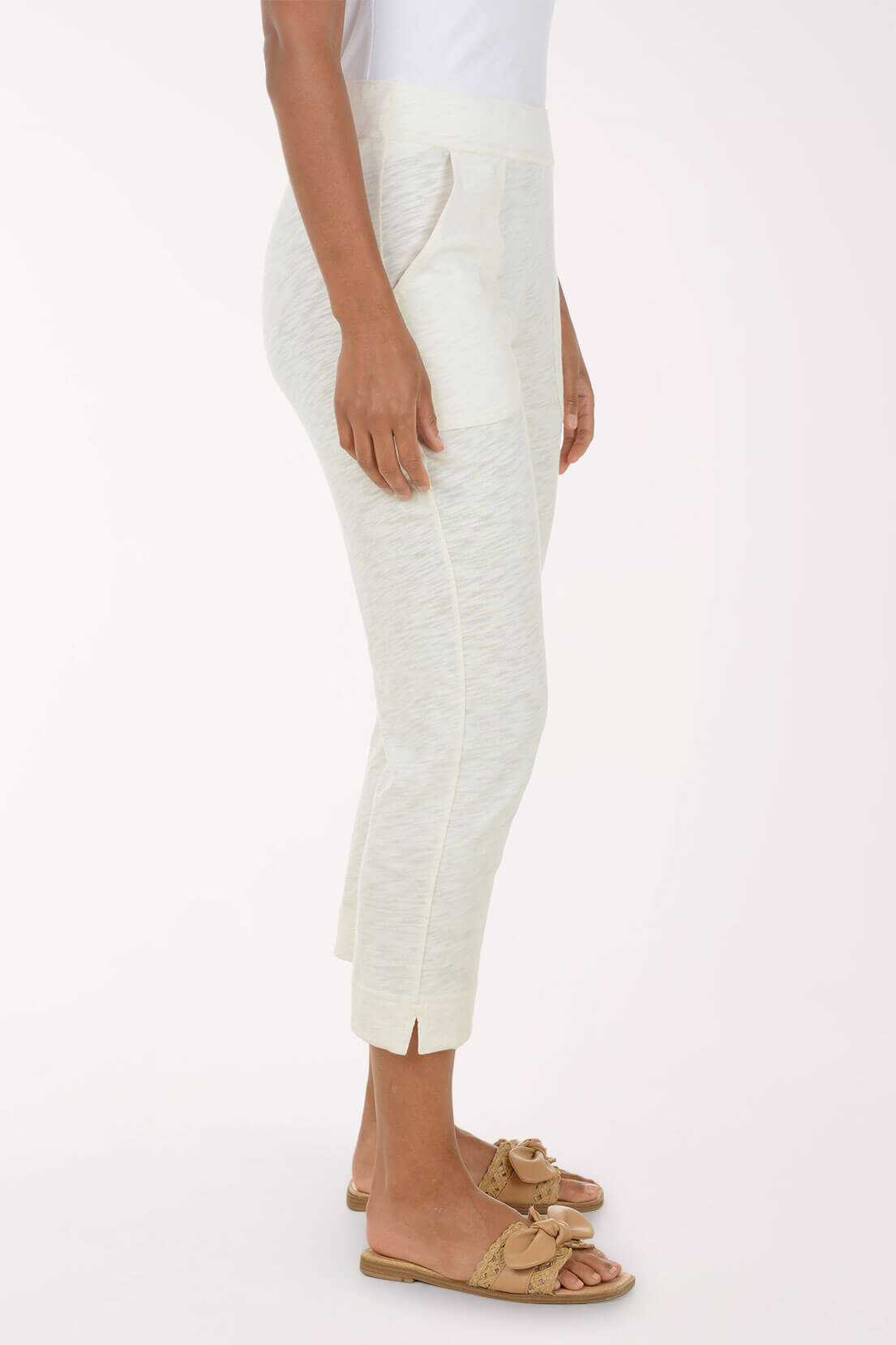 A side-profile view of a person wearing textured off-white cropped pants with side pockets and tan slide sandals against a plain light background.