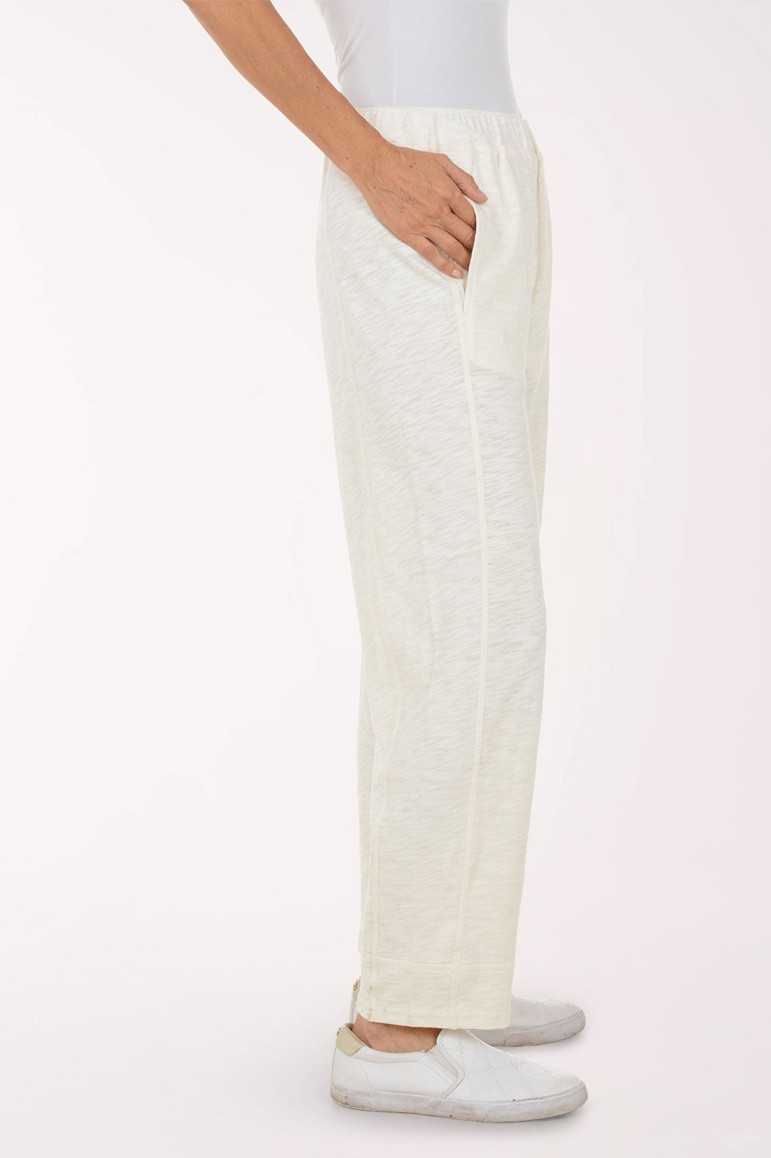 A person wearing loose, high-waisted off-white linen pants with side pockets and white slip-on shoes, shown against a plain light background.