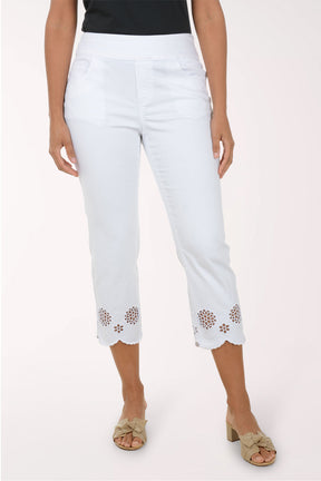 Woman wearing a blue embroidered top and white pants on a white background