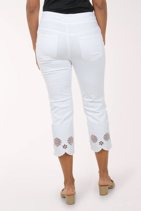 Woman wearing a blue embroidered top and white pants on a white background