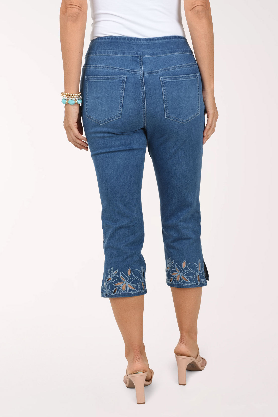 A back view of the denim capri pants showing the back pockets and floral cut-out details at the hem.