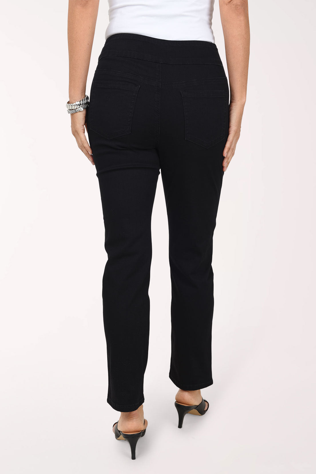 A back view of black straight-leg denim pants showing the back pockets, worn with black strappy heels.