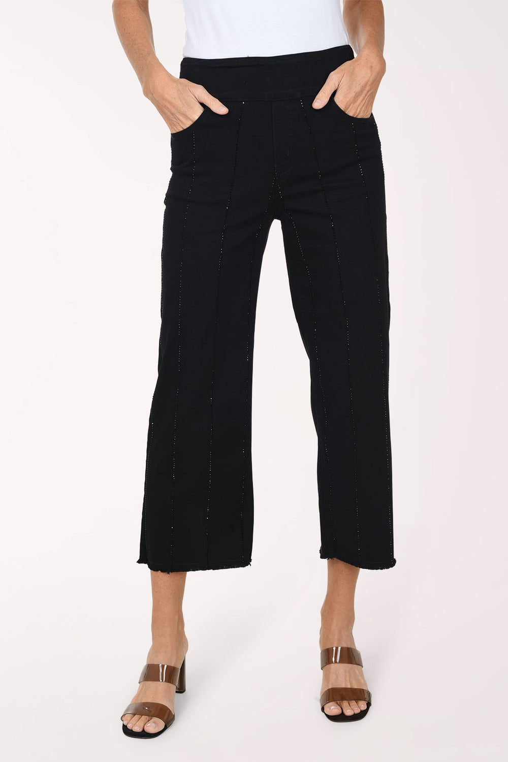 A front view of black wide-leg cropped denim pants with subtle vertical rhinestone stripes and a frayed hem, worn with a white top and clear-strap heeled sandals.