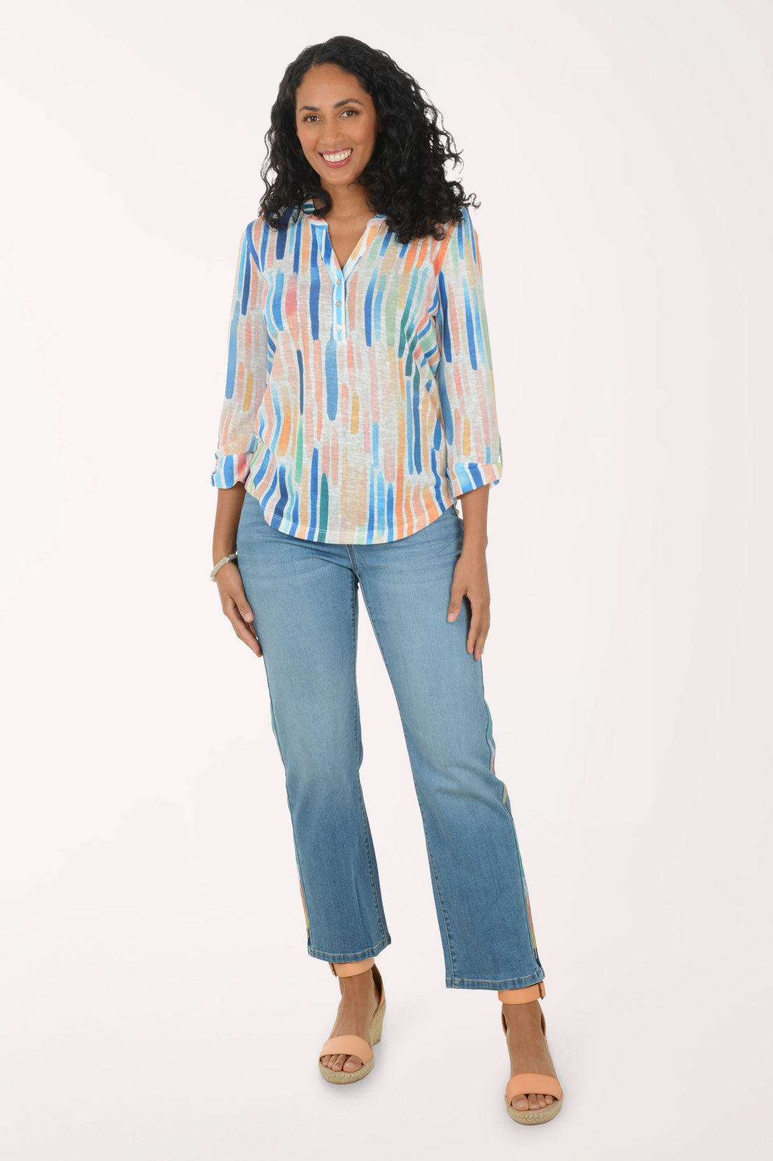 Woman wearing a colorful striped blouse and blue jeans on a white background