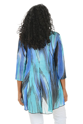 Woman wearing a blue and green patterned kimono-style jacket on a white background. Back shot.