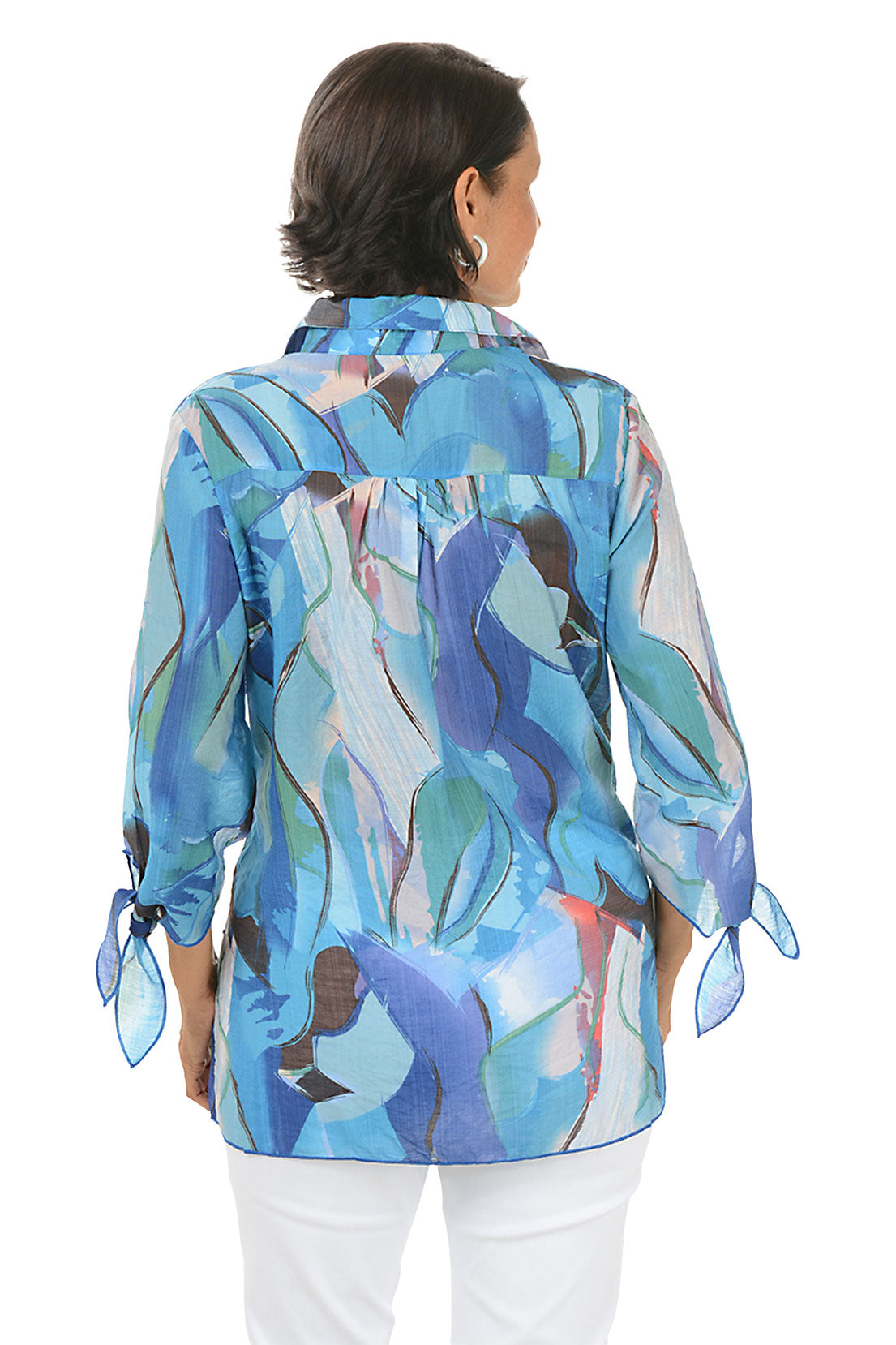 Woman wearing a colorful patterned blouse with white pants on a white background. Back shot.