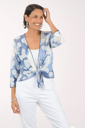 Woman wearing a blue and white  patterned shrug over a white top and pants on a white background