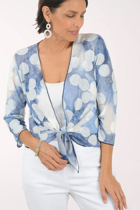 Woman wearing a blue and white  patterned shrug over a white top and pants on a white background