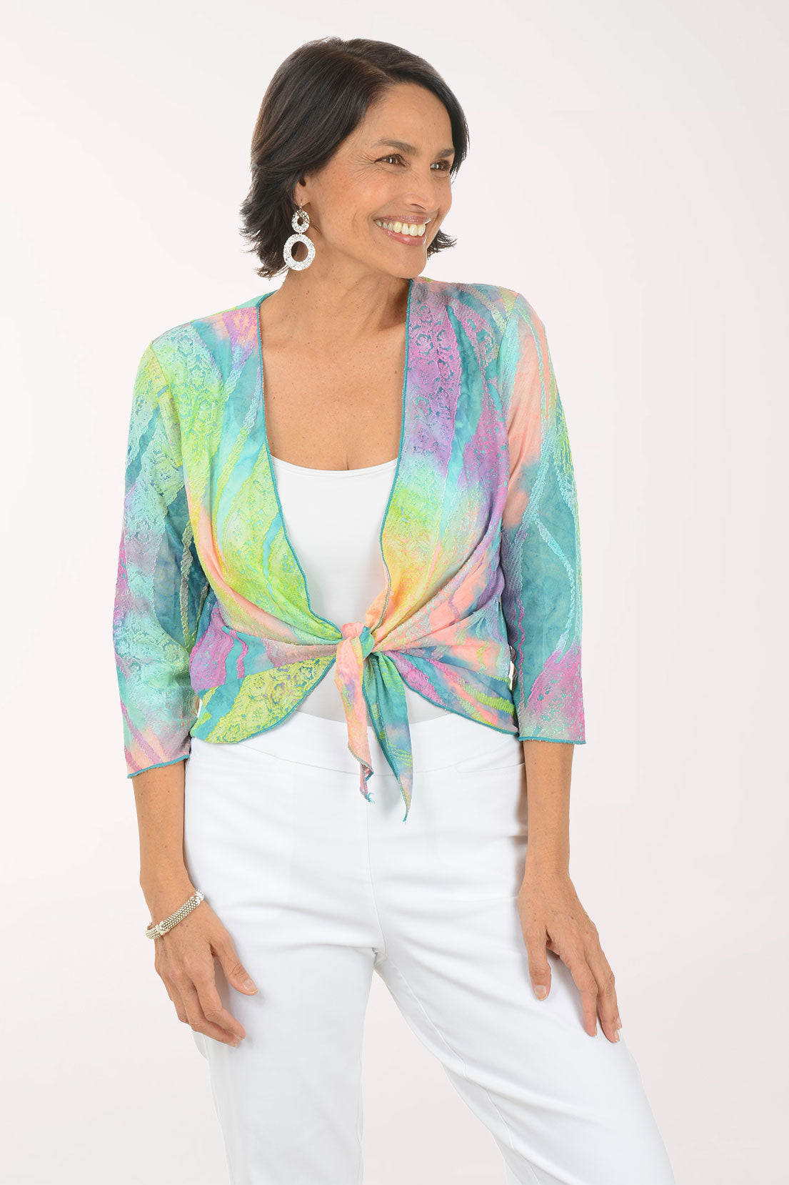 Woman wearing a multi colored patterned shrug over a white top and pants on a white background