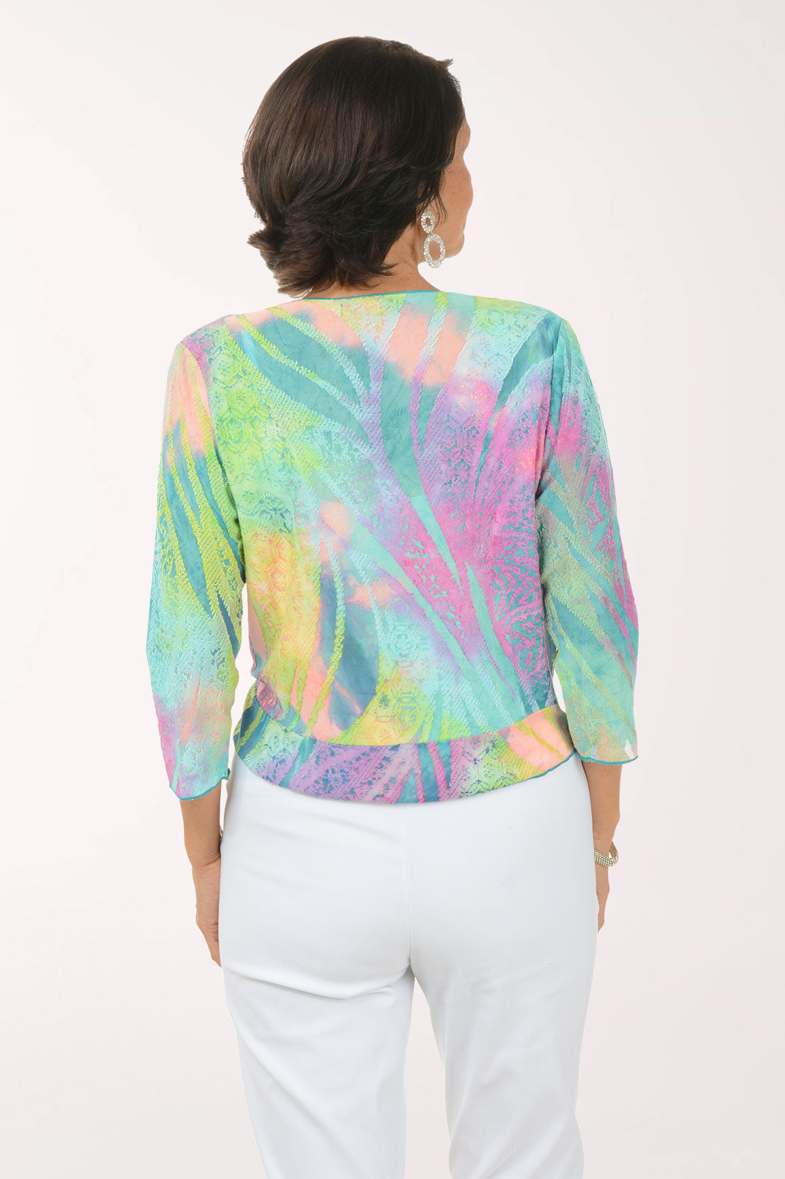 Woman wearing a multi colored patterned shrug over a white top and pants on a white background