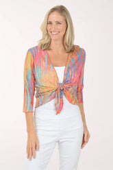 Woman wearing a multi colored patterned shrug over a white top and pants on a white background