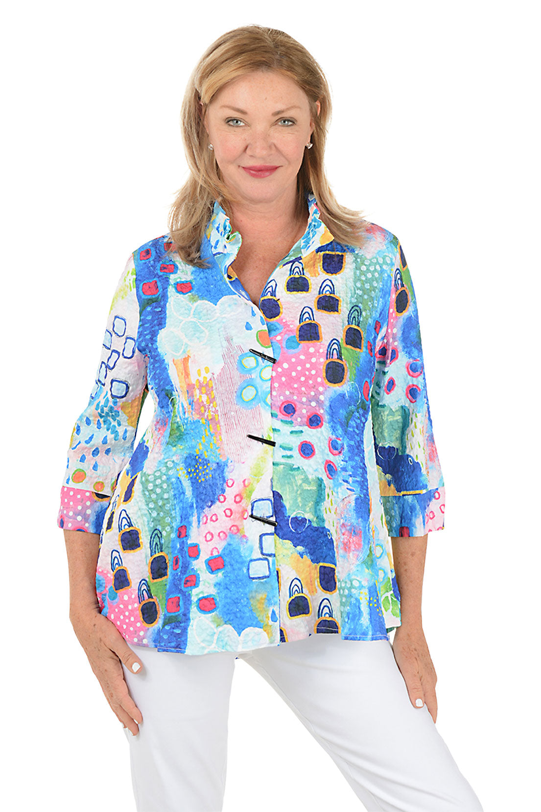 Woman wearing a colorful patterned blouse with white pants on a white background.