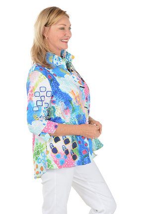 Woman wearing a colorful patterned blouse with white pants on a white background. Side shot.