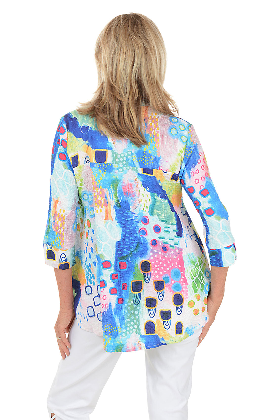 Woman wearing a colorful patterned blouse with white pants on a white background. Back shot.