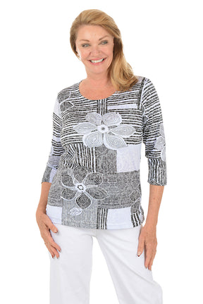 Woman wearing a black and white patterned top with floral designs on a white background. Second front shot.