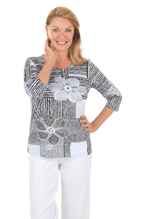 Woman wearing a black and white patterned top with floral designs on a white background.