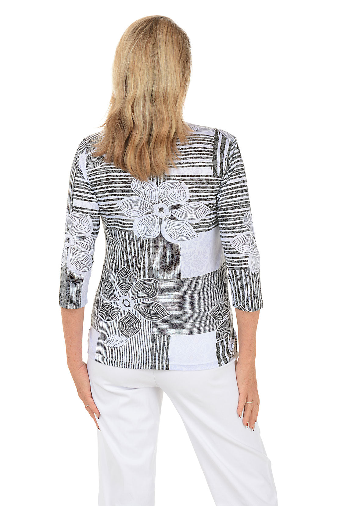 Woman wearing a black and white patterned top with floral designs on a white background. Back shot.