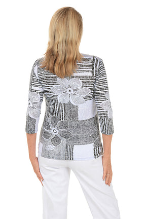 Woman wearing a black and white patterned top with floral designs on a white background. Back shot.