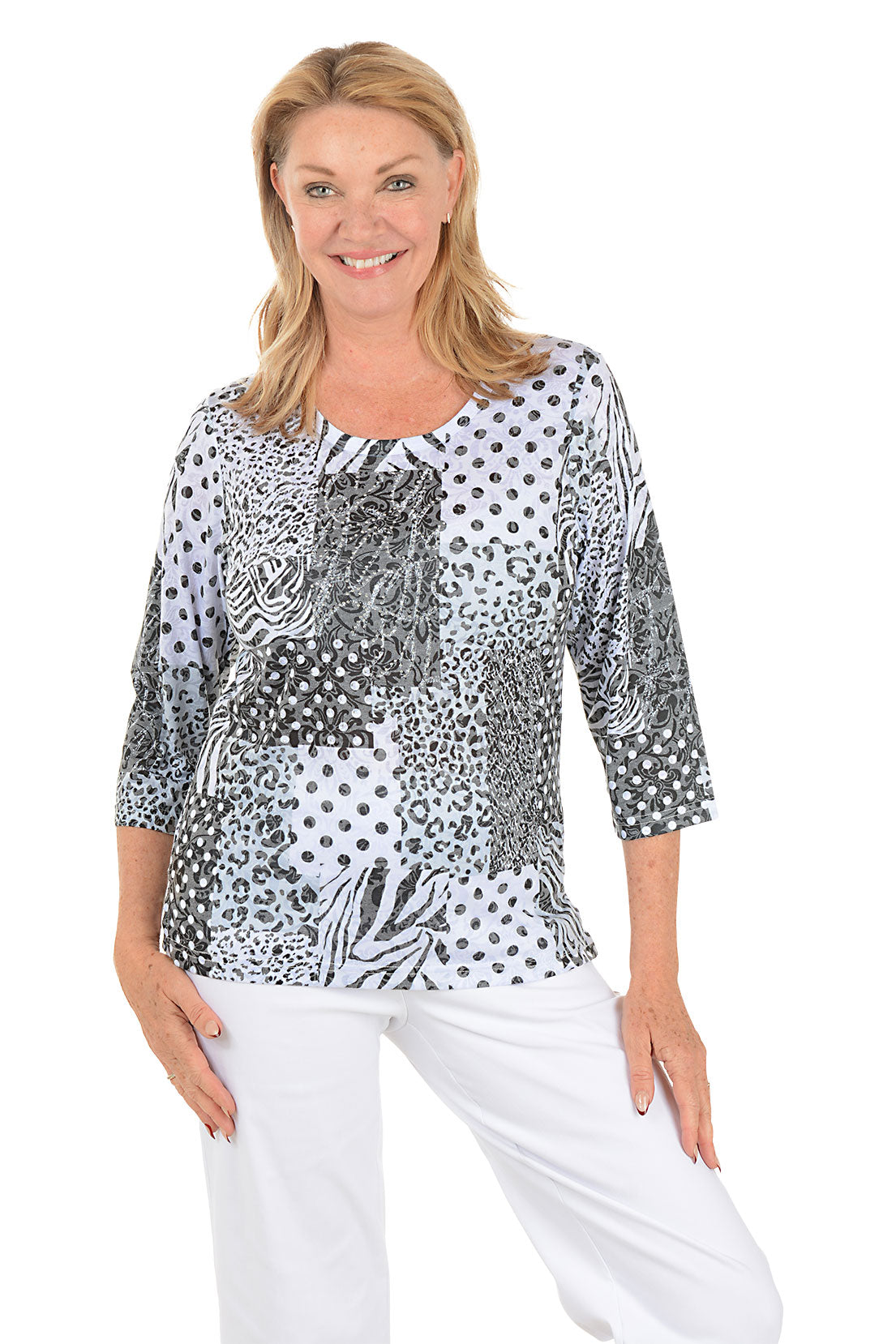 Woman wearing a patterned top and white pants on a white background.