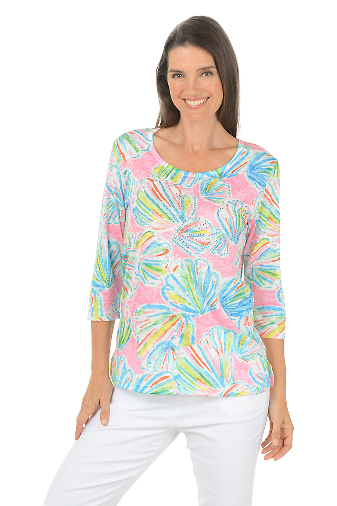 Woman wearing a colorful patterned top with white pants on a white background.