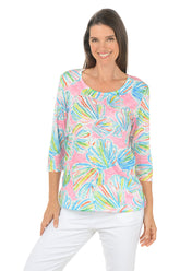 Woman wearing a colorful patterned top with white pants on a white background.