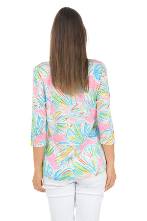 Woman wearing a colorful patterned top with white pants on a white background. Back shot.