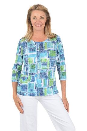 Woman wearing a colorful patterned top and white pants on a white background.