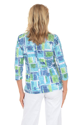 Woman wearing a colorful patterned top and white pants on a white background. Back shot.