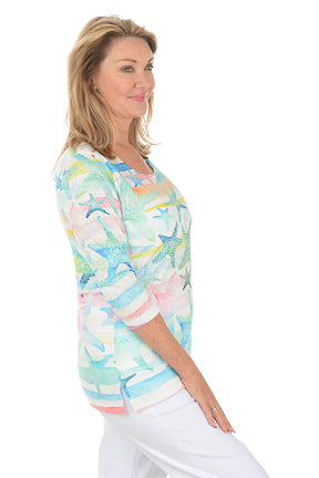 Woman wearing a colorful starfish-patterned top on a white background. Side shot.