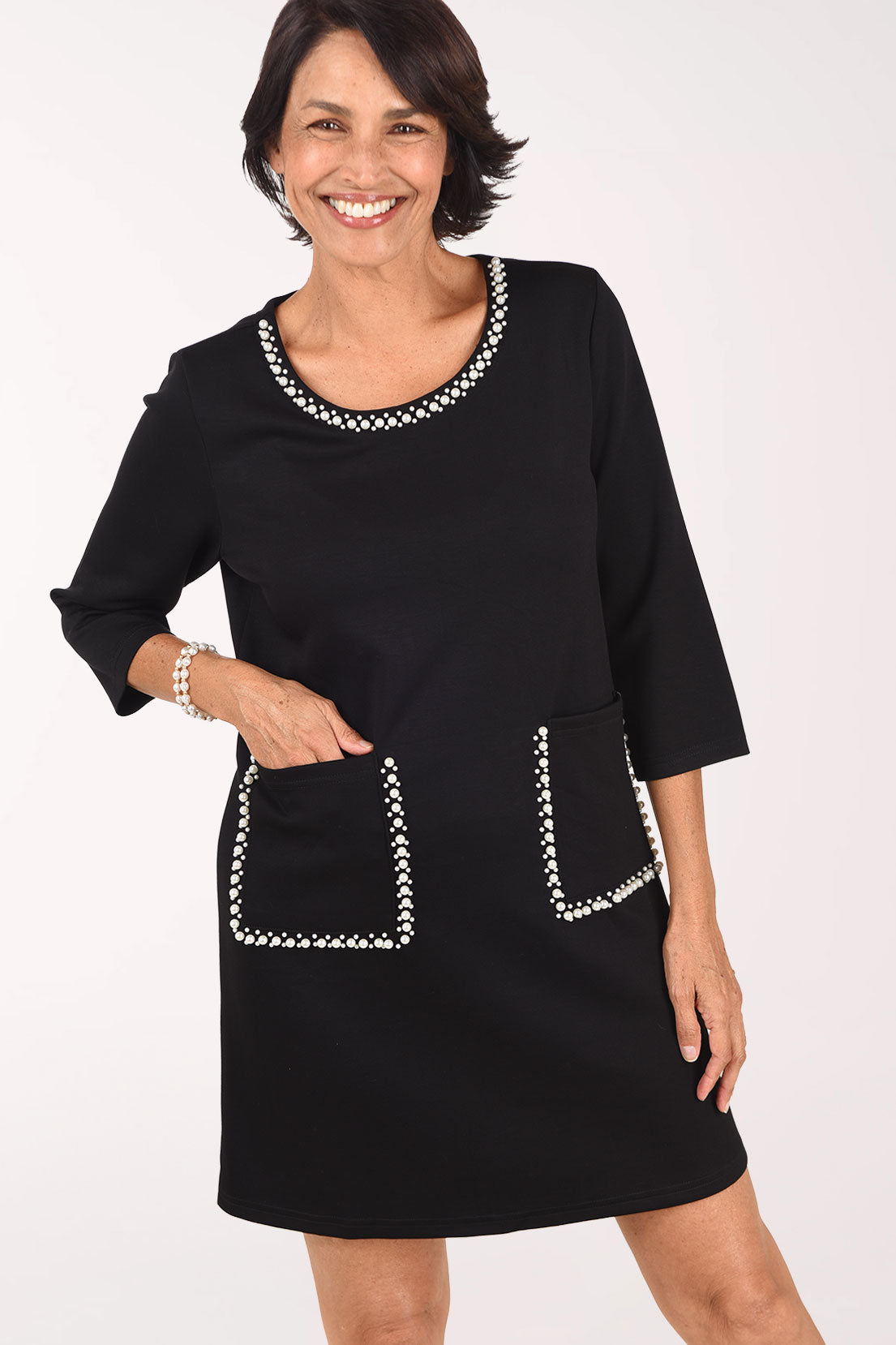 Close-up front view of the black Pearl Trim Pocket Dress showing the pearl-trimmed scoop neckline and the two patch pockets outlined in pearls, one hand resting in a pocket