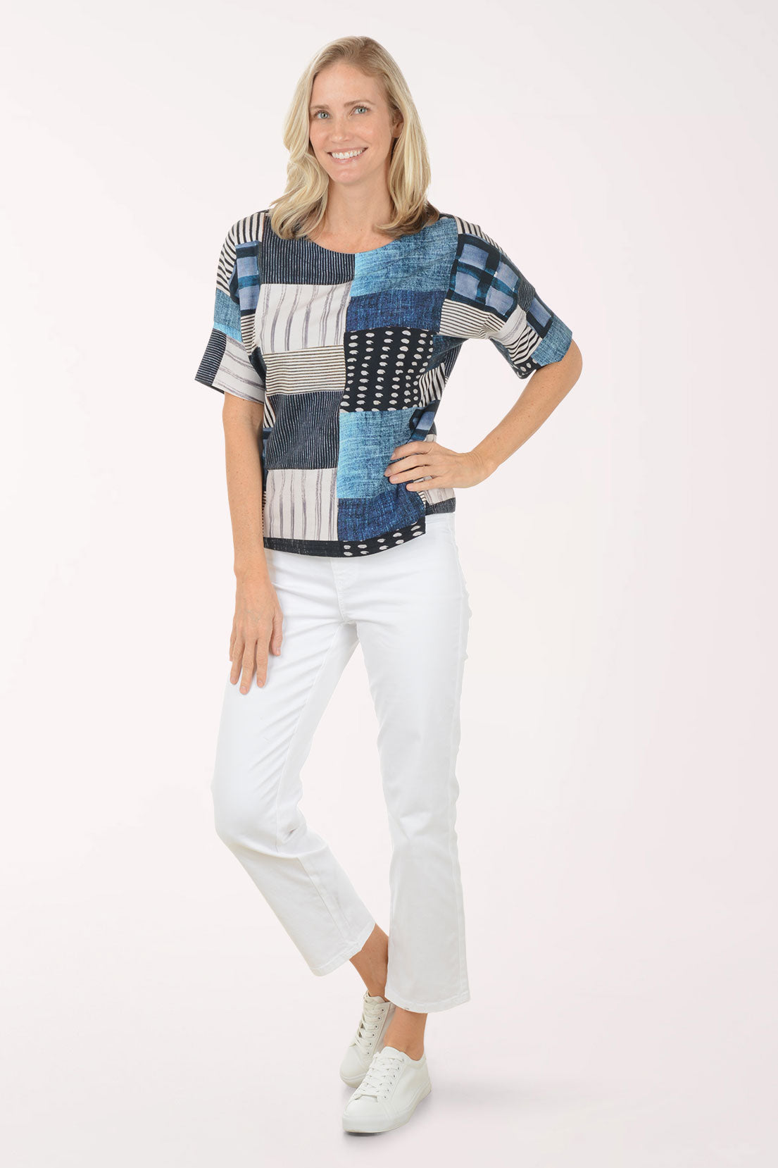 Woman wearing a patchwork shirt and white pants on a white background