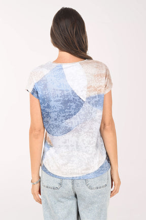 Woman wearing a blue and white patterned top with light jeans on a white background
