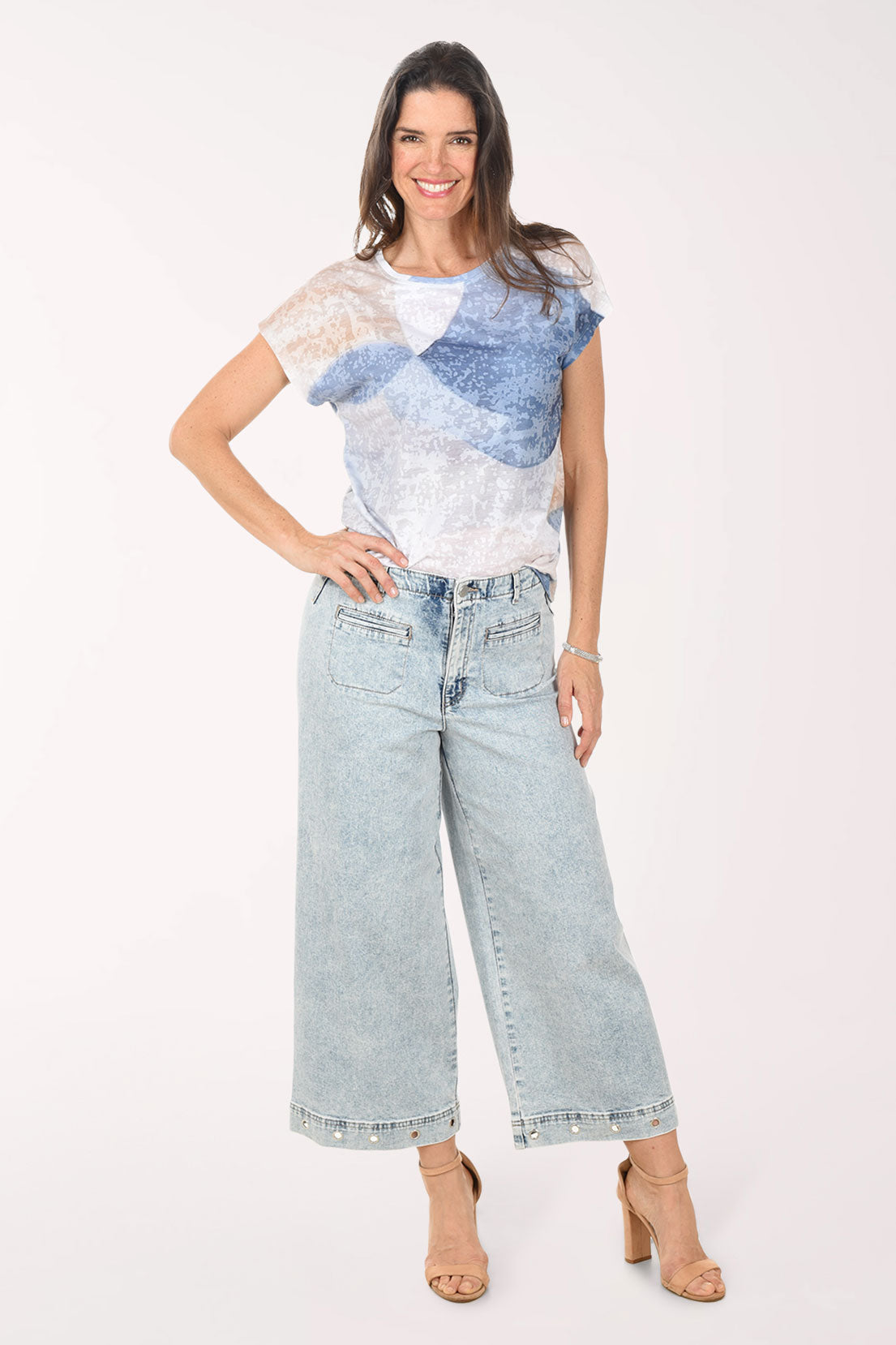 Woman wearing a white and blue patterned top with light blue jeans on a white background