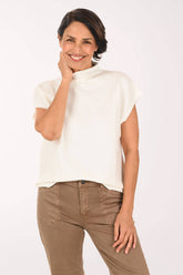 A woman modeling a white ribbed short-sleeve mock neck top paired with brown pants, photographed against a clean white studio background.