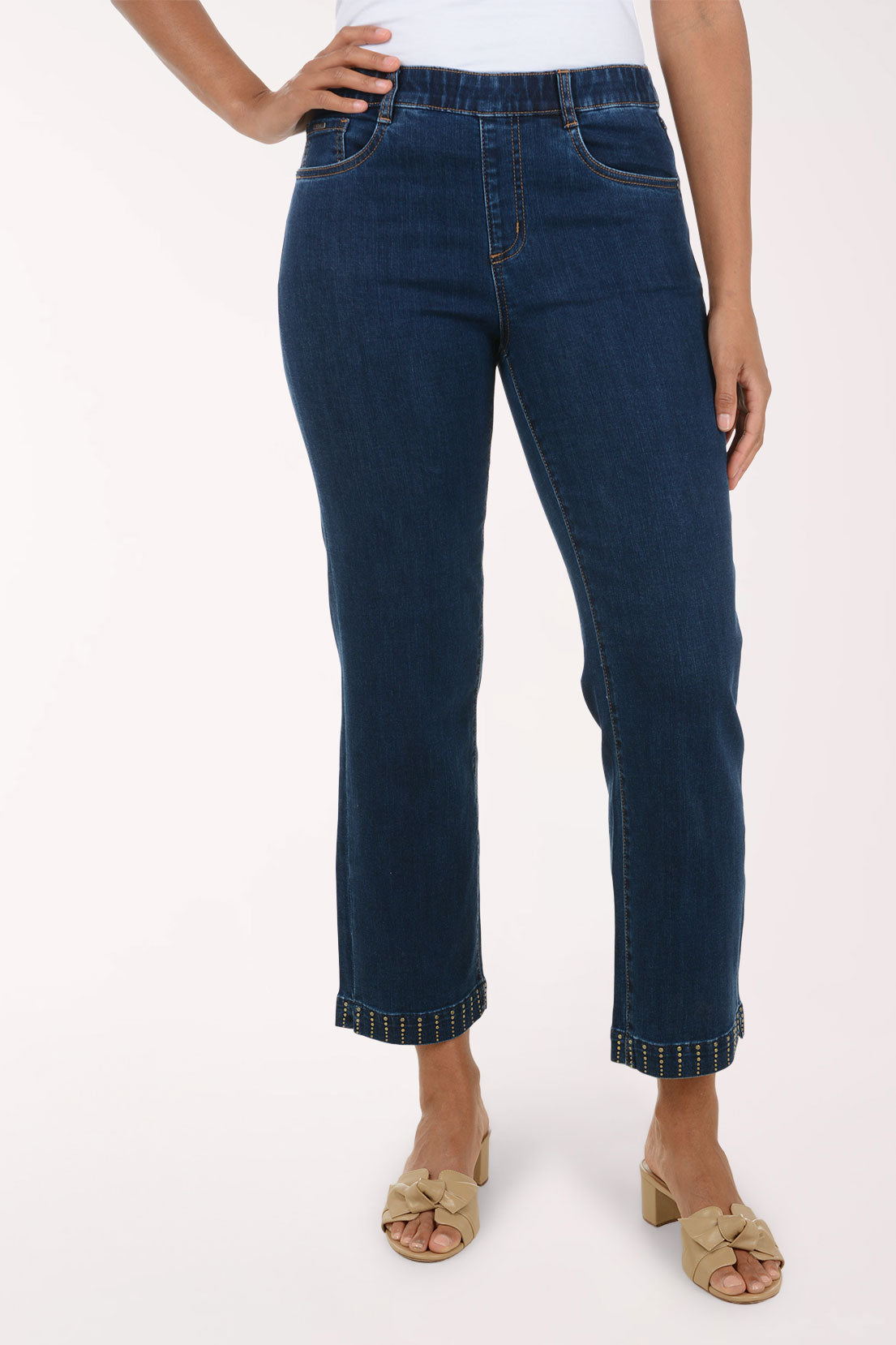 A model wearing dark blue cropped jeans with rolled hems and decorative contrast stitching, paired with beige slide sandals against a plain white studio background.