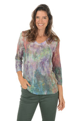 Woman wearing a v-neck 3/4 sleeve colorful tie-dye shirt and green pants on a white background.