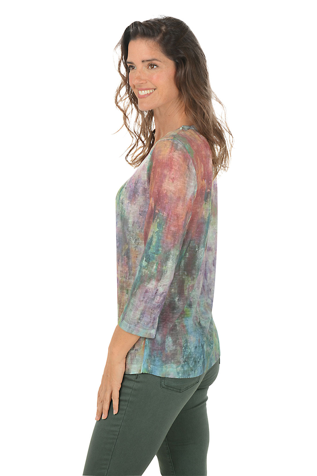 Woman wearing a v-neck 3/4 sleeve colorful tie-dye shirt and green pants on a white background. Side shot.