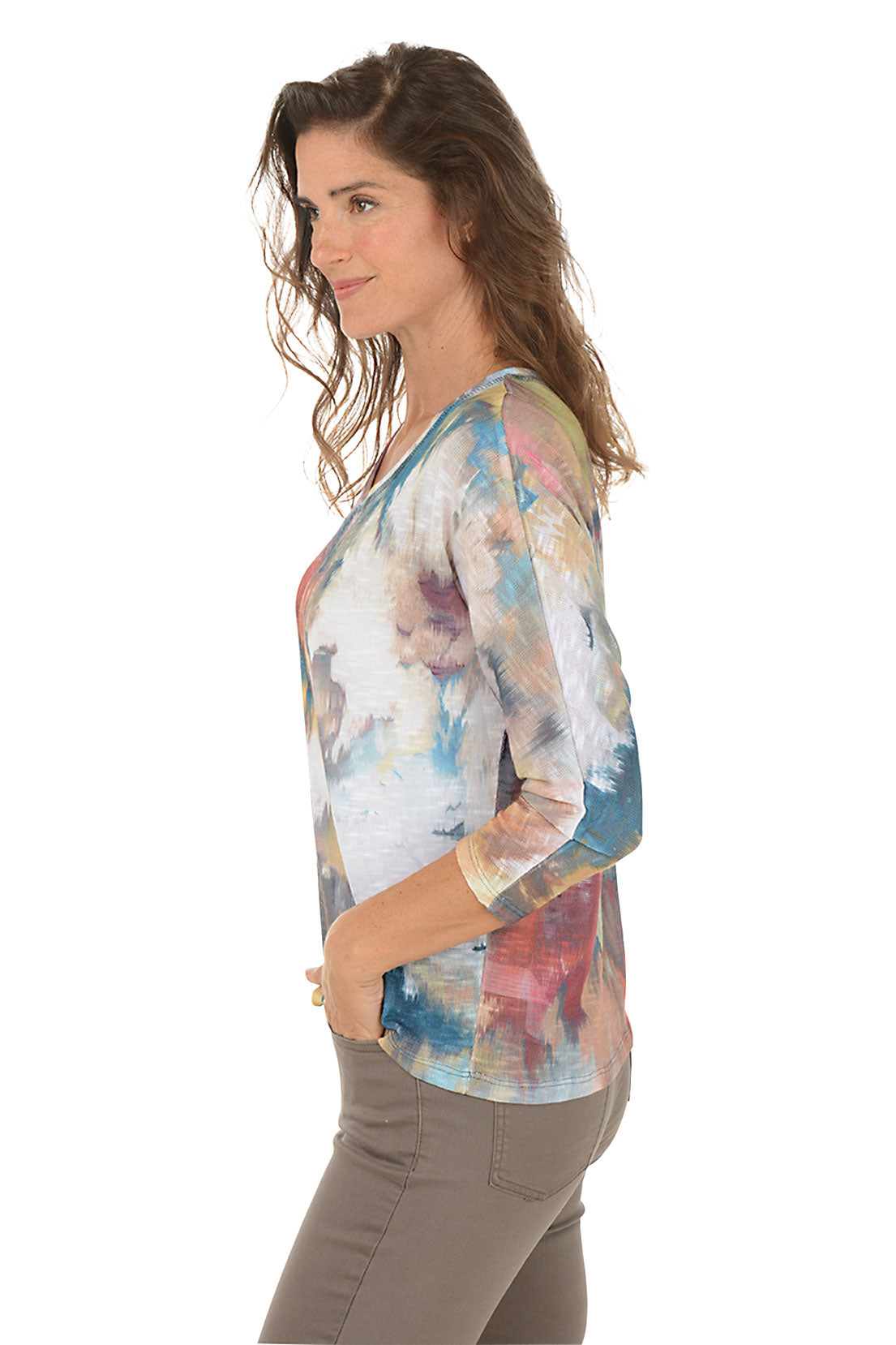 Woman wearing a scoop neck 3/4 sleeve colorful tie-dye shirt with arms crossed on a white background. Side shot.