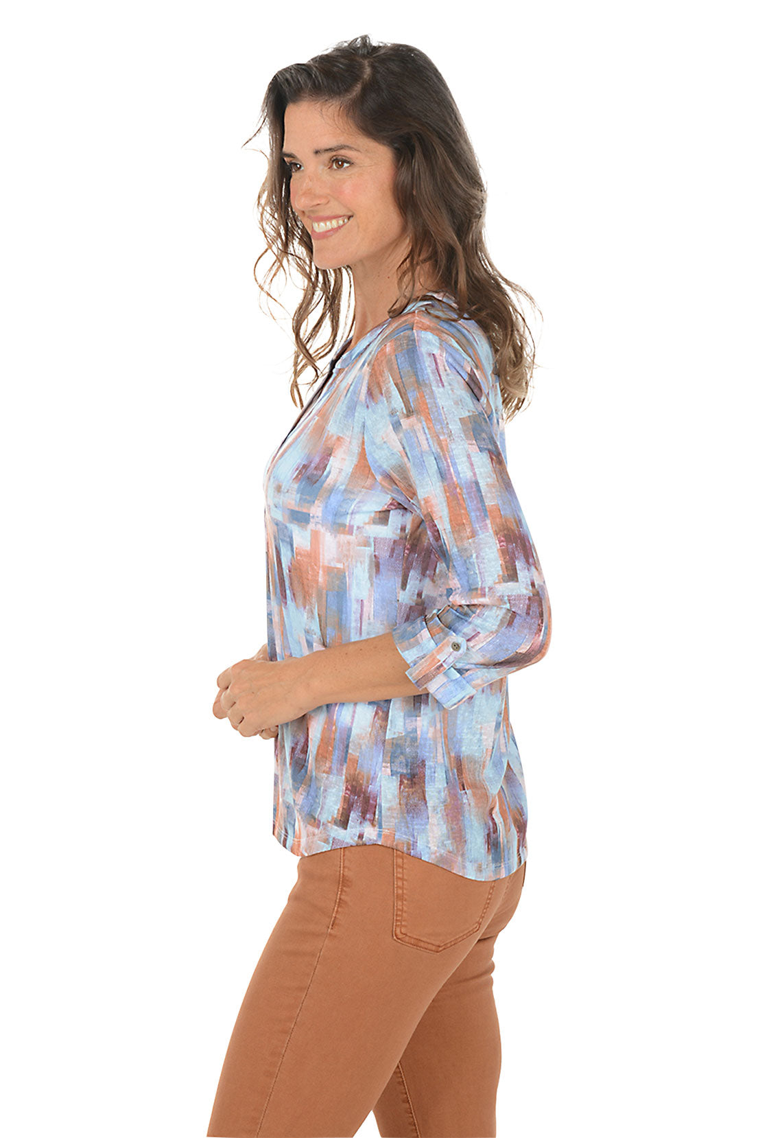 Woman wearing a patterned blouse with brown pants on a white background. Side shot.