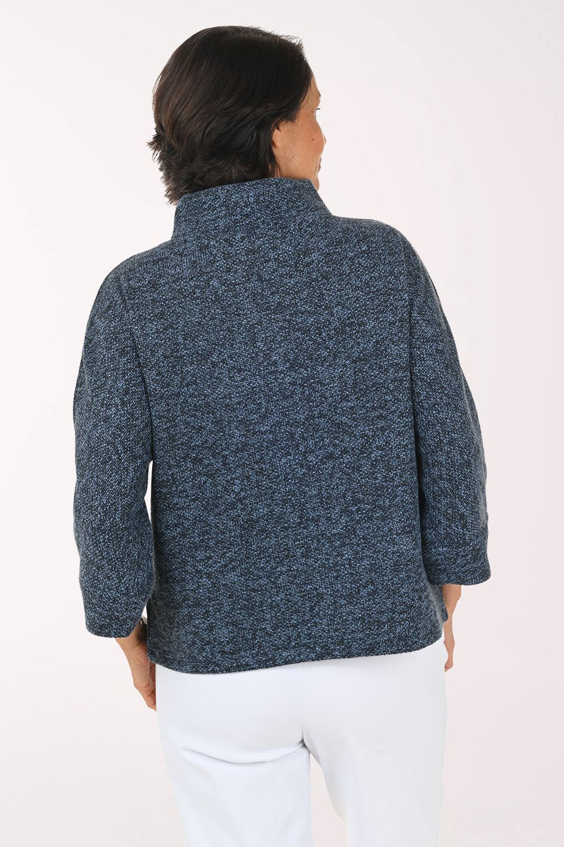 A person shown from the back wearing a textured, heathered navy blue knit jacket with white pants, against a plain light background.