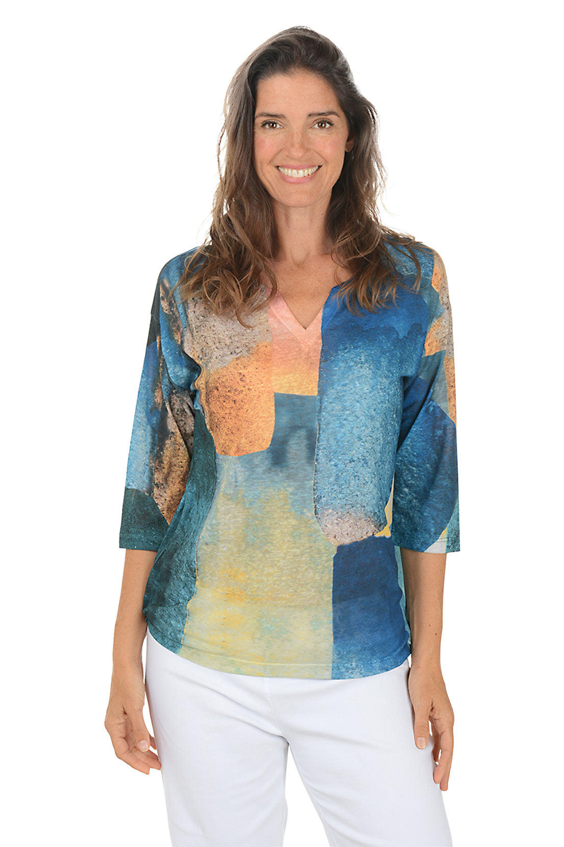 Woman wearing a colorful patterned top with white pants on a white background.