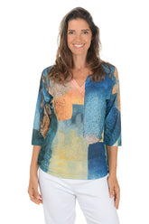 Woman wearing a colorful patterned top with white pants on a white background.