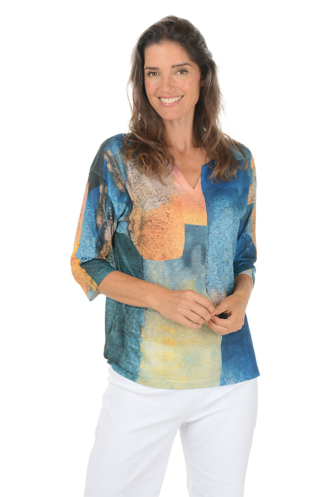 Woman wearing a colorful patterned top with white pants on a white background. Second front shot.
