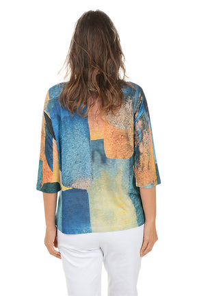 Woman wearing a colorful patterned top with white pants on a white background. Back shot.