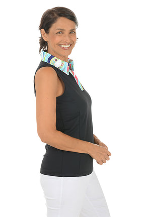 Woman wearing a black sleeveless top with a colorful collar and white pants on a white background. Side shot.