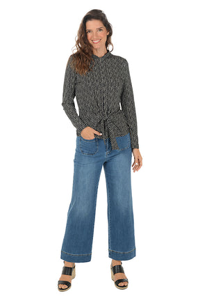 Woman wearing a patterned top and blue jeans on a white background.