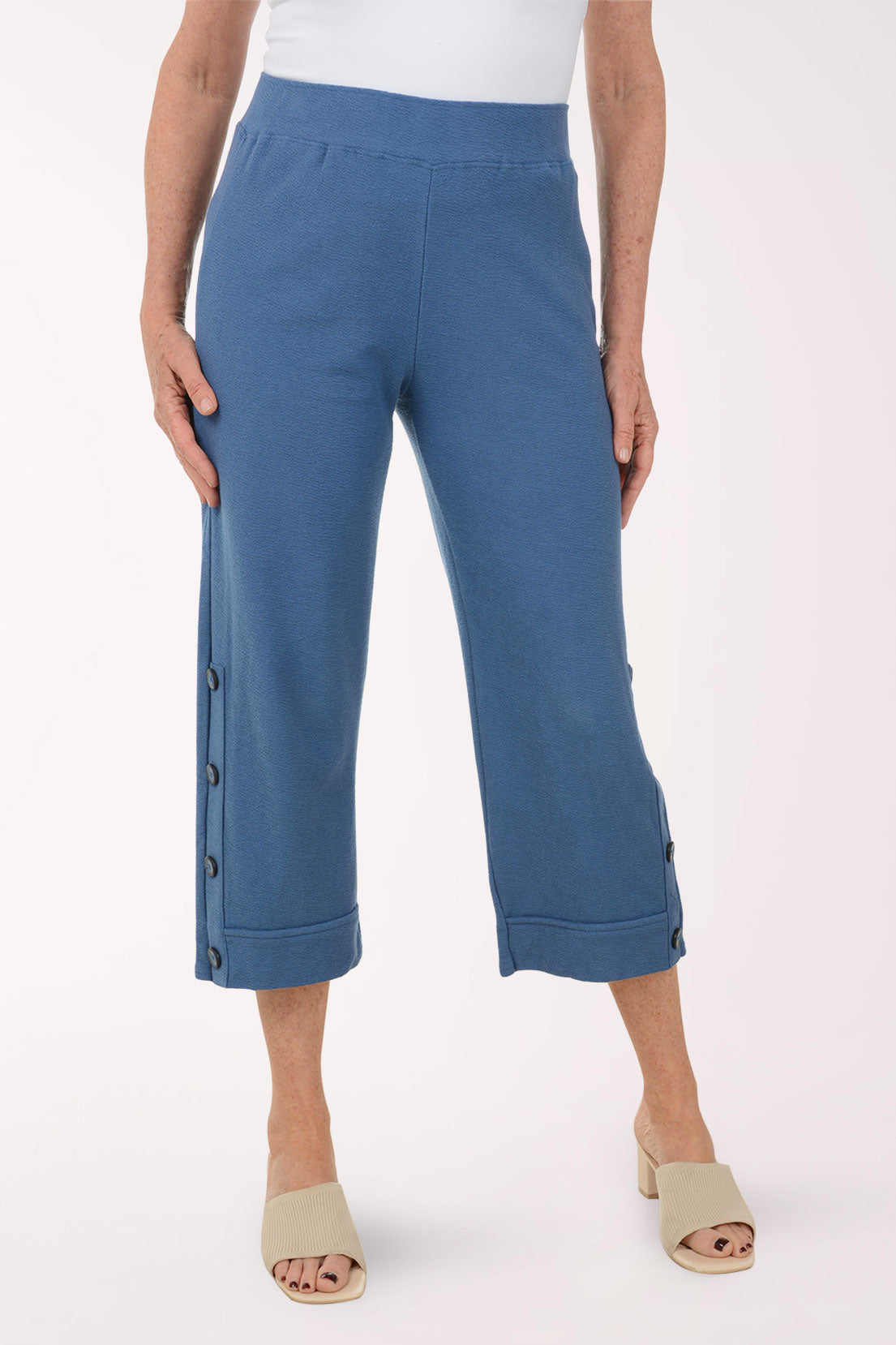 Blue pants with button details worn by a person on a white background