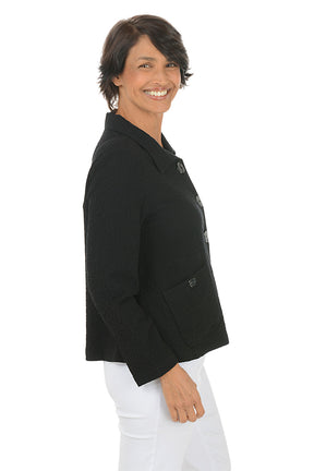 Woman wearing a black collared jacket with button details on a white background. Side shot.