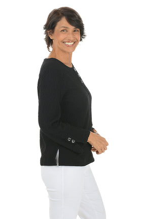 Woman wearing a black long-sleeve top with button details on a white background. Side shot.