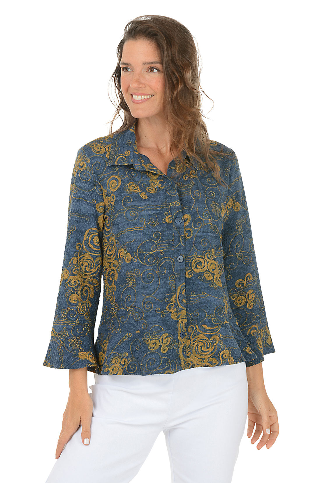 Woman wearing a blue and gold patterned blouse with white pants on a white background.